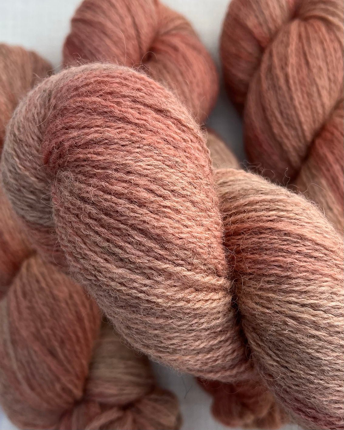 Skeins of soft pink toned variegated sustainable British 4ply wool naturally dyed with plants for knitting