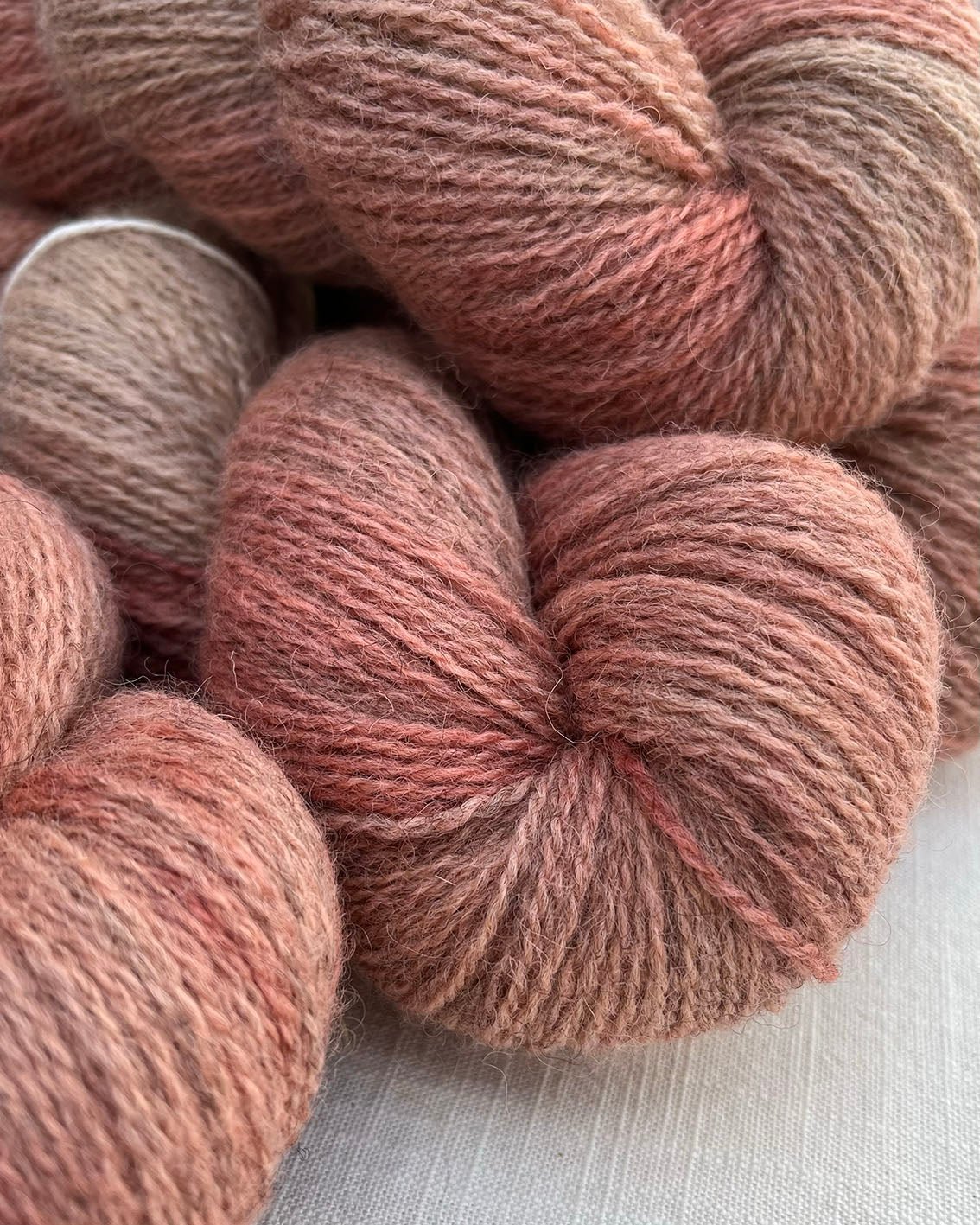 Skeins of soft pink toned variegated sustainable British 4ply wool naturally dyed with plants for knitting